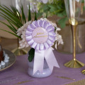Cocarde Joyeux Anniversaire lilas et or avec rosace en ruban satiné et médaillon à confettis dorés Cocarde Joyeux Anniversaire lilas et or avec rosace en ruban satiné et médaillon à confettis dorés