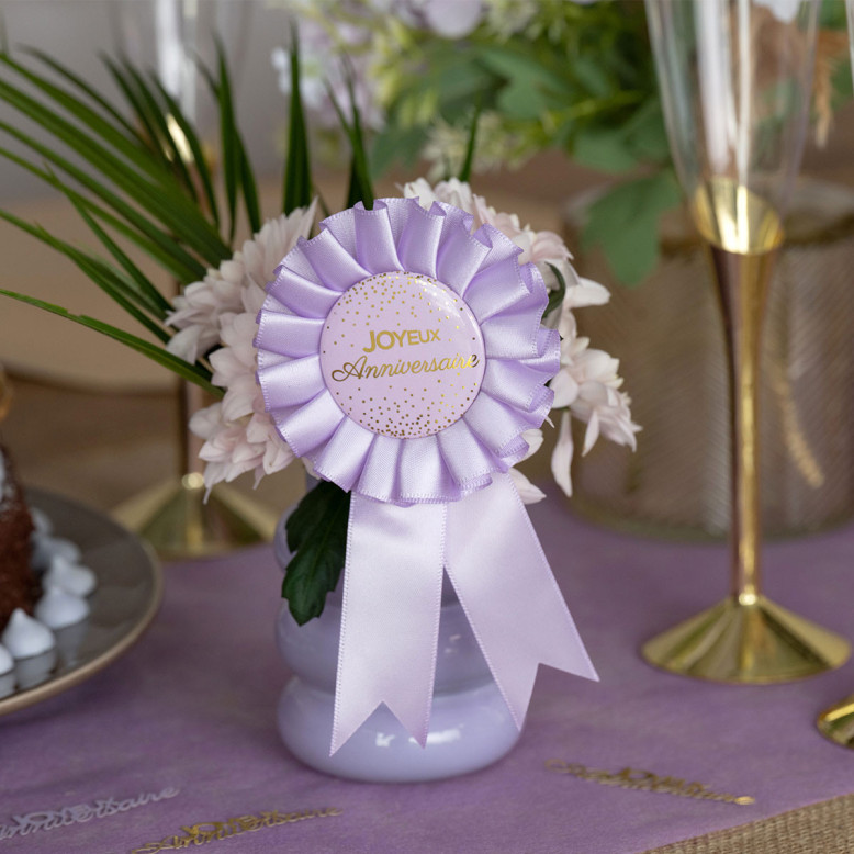 Cocarde Joyeux Anniversaire lilas et or avec rosace en ruban satiné et médaillon à confettis dorés Cocarde Joyeux Anniversaire lilas et or avec rosace en ruban satiné et médaillon à confettis dorés