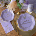 Assiette Joyeux Anniversaire lilas et or 18 cm en carton avec bord festonné, nœud et confettis dorés Assiette Joyeux Anniversaire lilas et or 18 cm en carton avec bord festonné, nœud et confettis dorés